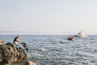 2015. Lesvos. Greece. Greek man helps Syrian refugees out of the water.  The engine of a boat carrying around 50 Syrians fails, close to the Greek coast. When the coastguard arrives, some refugees jump into the water out of fear and try to swim to the shore. Eventually, the tide carries the boat in, with the remaning Syrians.